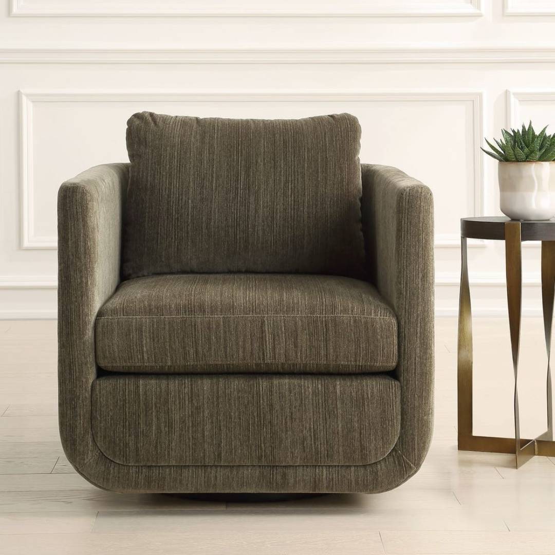 The Solana Swivel Accent Chair in green chenille fabric, featuring a boxy shape, sits on a light wood floor beside a gold side table with a white marble top and potted succulent, set against white decorative wall paneling.