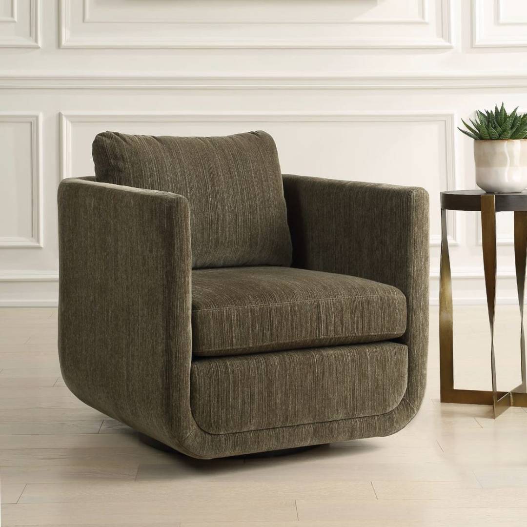 The Solana Swivel Accent Chair in green chenille, with sculptural curves, sits on light wood flooring beside a gold metal side table holding a white pot and succulent, set against white paneled walls.