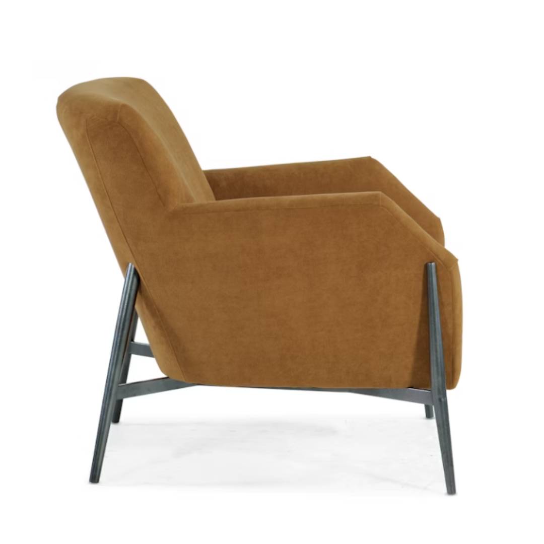 A side view of the Sienna Luxe Custom Accent Chair features cognac upholstery, angular armrests, a slightly reclined backrest, and thin black metal legs forming a geometric base. The chair is set against a plain white background.