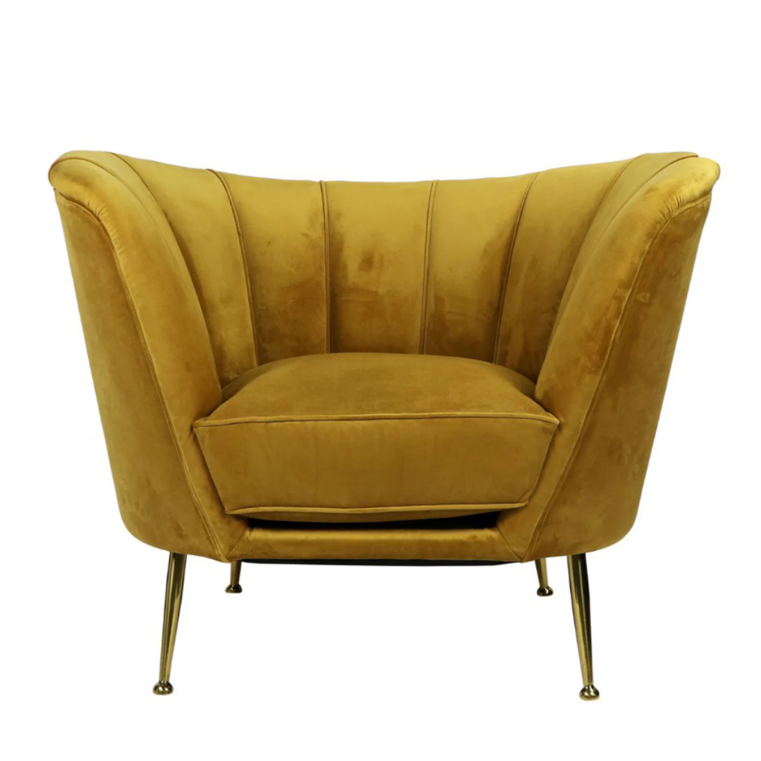 The Calvierre Channel-Tufted Velvet Chair is a plush mustard yellow piece with a wide, curved backrest and elegant channel-tufting, featuring a thick cushioned seat and standing on four slender splayed brass legs for a modern yet luxurious look.