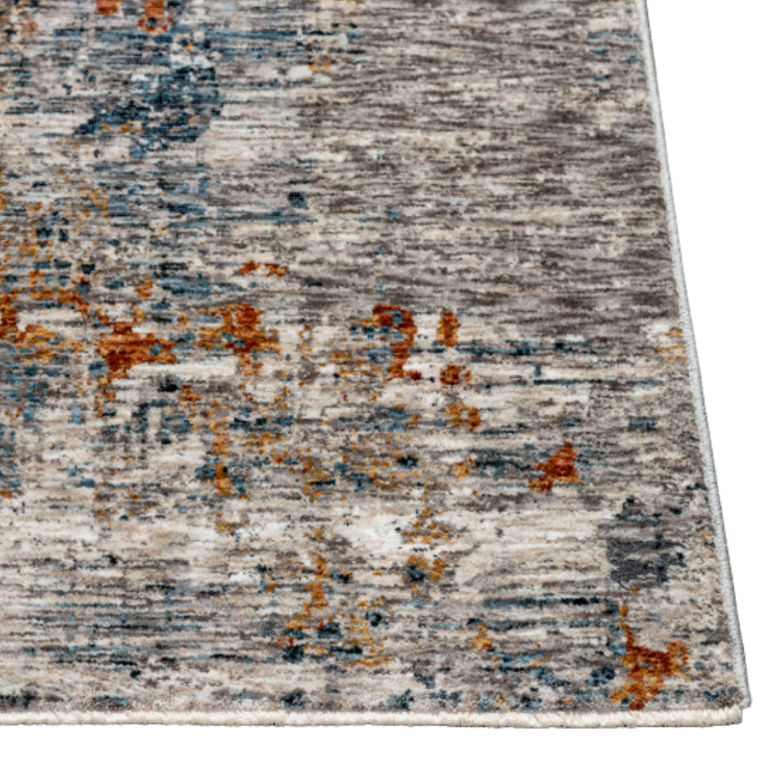 A close-up of the Candice Machine Woven Rug showcases its abstract pattern in gray, beige, blue, and orange tones. The image highlights a corner of this rectangular medium pile rug, revealing its textured and weathered look.