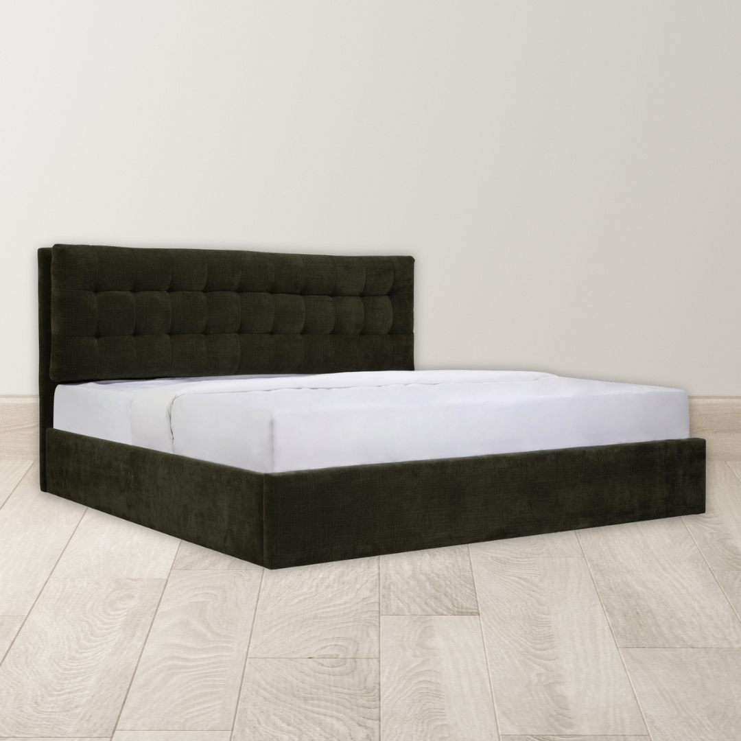 The Corveline Green Storage Bed, featuring a modern hydraulic lift, dark tufted headboard, and upholstered base with a white mattress, stands in a minimally decorated room with light wood floors and plain off-white walls. No other furniture or decor is present.