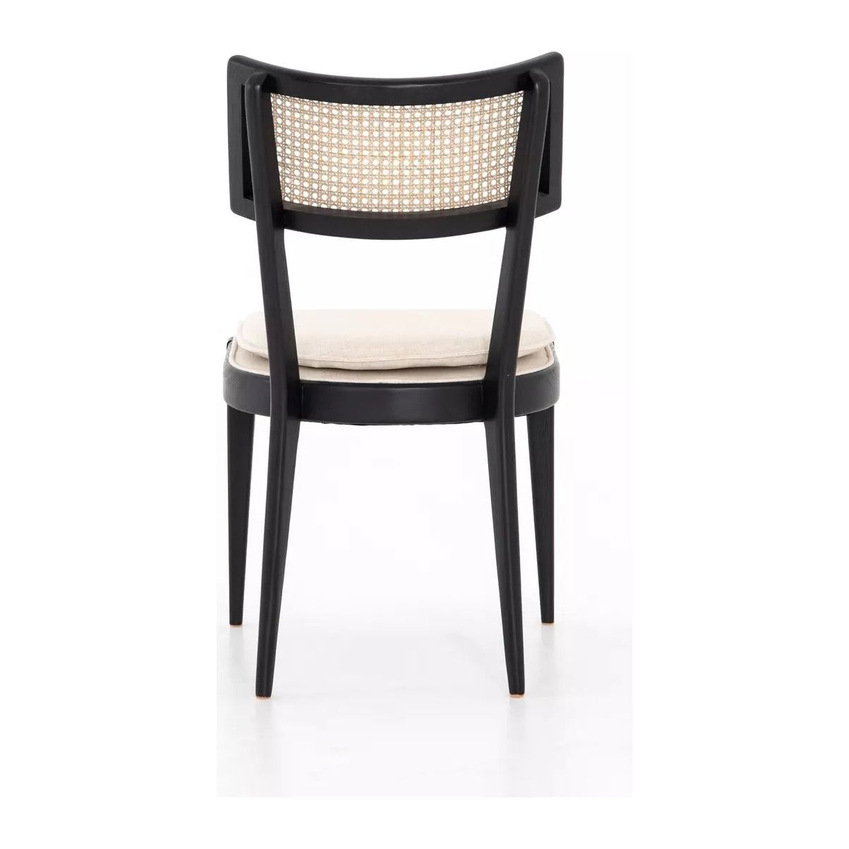 A Britt Dining Chair with an ebony-finished nettlewood frame, viewed from the back. The chair features a cane webbed backrest and a light beige cushioned seat made of high-performance linen-blend seating. The design is minimalist with four sleek, tapered legs, presenting a mix of modern and traditional styles. The background is white.