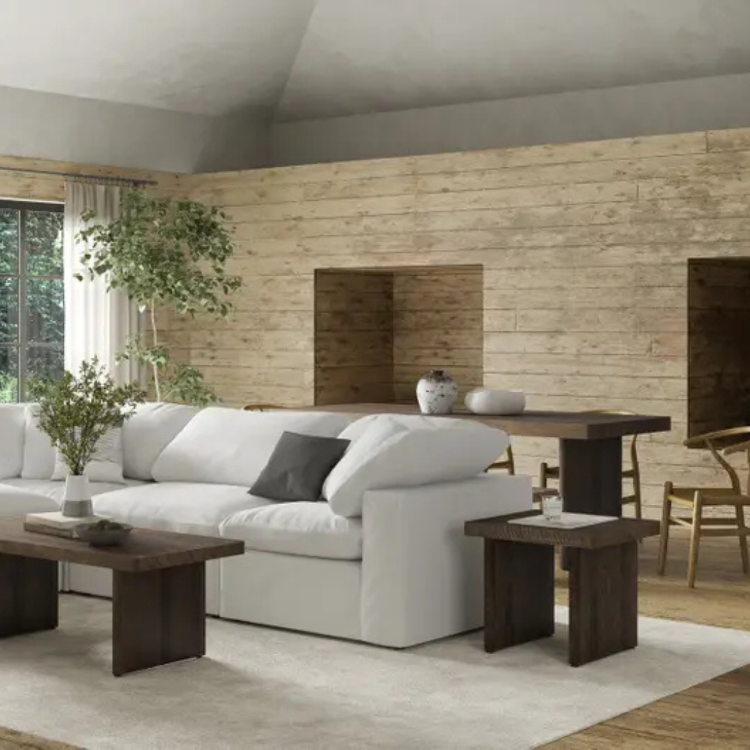 A modern living room features a white sectional sofa, the Monte Wood Side Table in driftwood finish, a dining table with matching chairs, potted plant, decorative vases, light rug, large windows, and wood-paneled walls with alcoves.