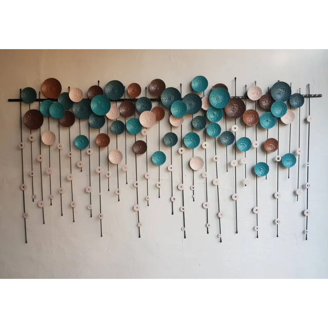 The Metallo Wall Art Sculpture showcases circular, textured discs in turquoise, brown, white, and copper on cross rods. Smaller discs hang below for a cascading effect. Display it on a white wall to add modern decor elegance to your space.