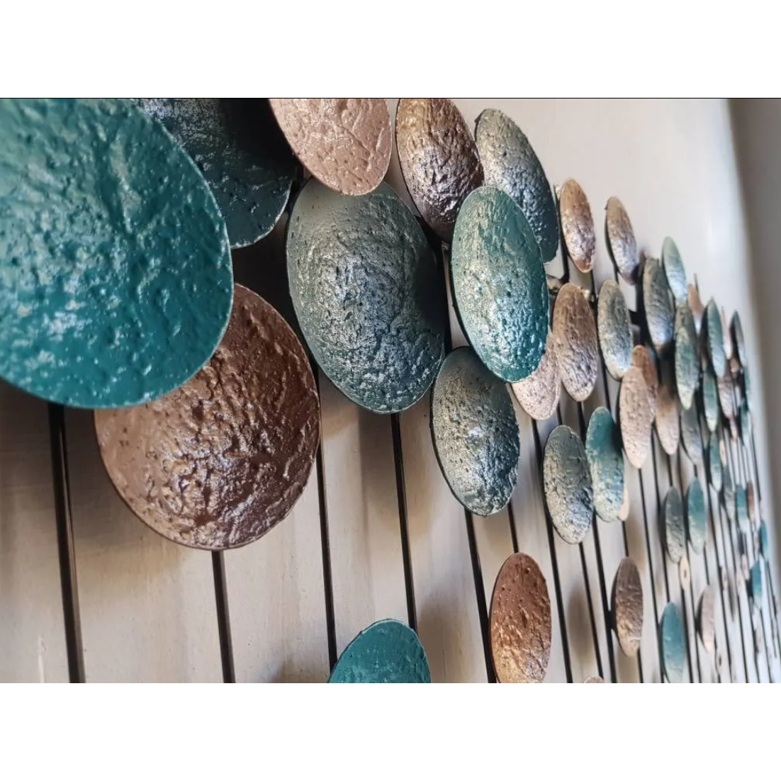 The Metallo Wall Art Sculpture showcases metallic circular discs in turquoise, copper, and bronze, arranged staggered and overlapping on thin rods to create a dynamic, tactile effect.