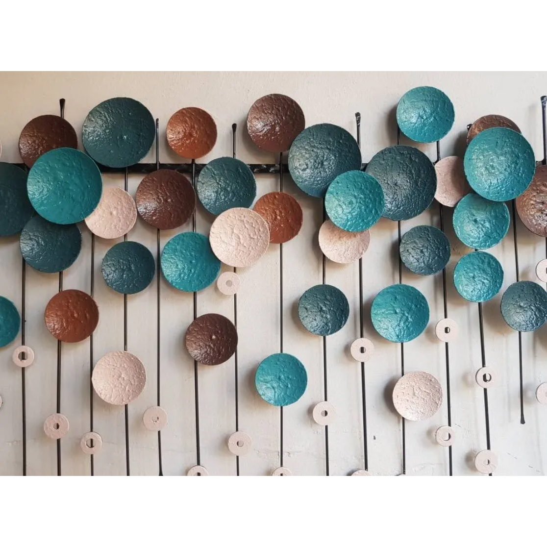 The Metallo Wall Art Sculpture features textured circular discs in teal, brown, and beige. Mounted on vertical and horizontal rods, it creates a layered 3D effect that enhances any modern decor.
