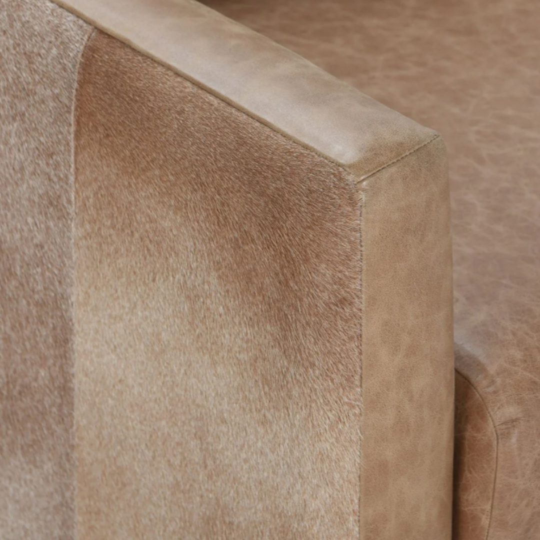 The Velancia Hide & Leather Swivel Chair features a close-up of modern glamour with two distinct textures: sleek top grain leather and light brown, hair-like fabric, divided by a clean line on the armrest to accentuate their contrasting elegance.