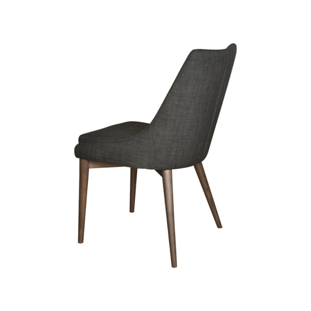 The Franny Dining Chair, Dark Gray, seen from a rear three-quarter angle, features a dark gray upholstered backrest and seat. With slim, slightly tapered wooden legs in a natural finish, this chair boasts a versatile design that's both elegant and minimalist. Its removable cover adds to its sleek and contemporary appeal.