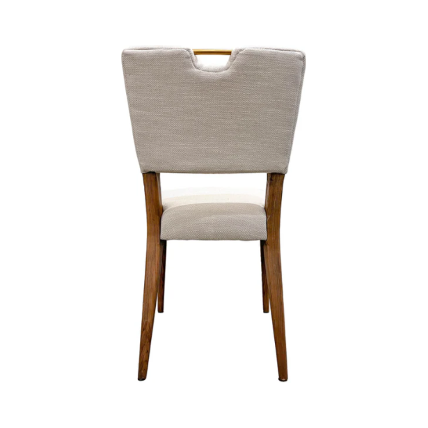The Arden Gold Handle Dining Chair features a beige upholstered backrest with a rectangular cutout and gold handle, solid ash wood legs in a natural finish, matching upholstered seat, and slightly tapered legs for a mid-century modern look.