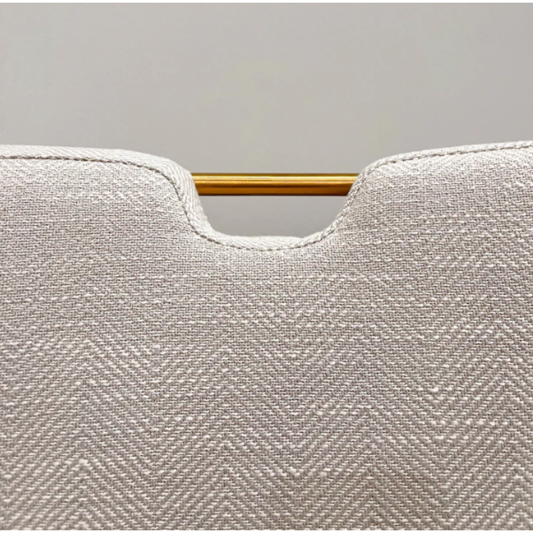 Close-up of the Arden Gold Handle Dining Chair's upholstered back in off-white herringbone fabric. A small notch reveals the gold handle, adding a refined touch. The background is plain light gray.