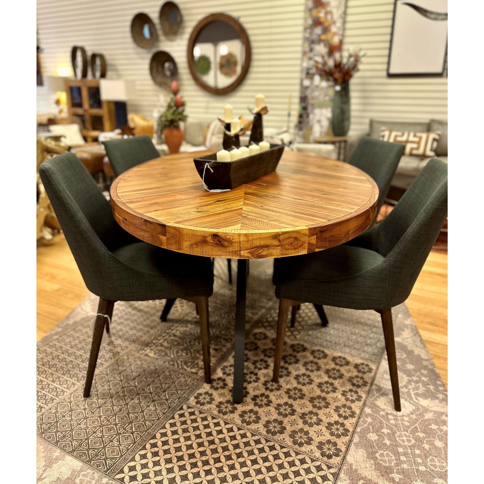 A round wooden dining table with a geometric pattern on its surface is surrounded by four Franny Dining Chairs, Dark Gray, upholstered with removable covers. The table sits on a patterned rug. In the background, various wall decor items, plants, and furniture pieces contribute to a cozy and stylish ambiance.