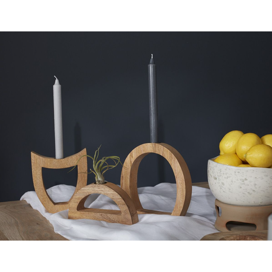 Modern geometric-designed Wooden Arch Candleholders with lunar phases feature a white and gray candle. A white cloth drapes the wooden surface, while a ceramic bowl filled with lemons on a stand sits to the right against a dark backdrop. An air plant adorns one holder.