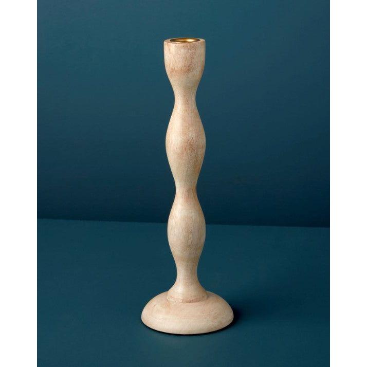 The Wood Candlestick stands upright on a flat teal surface, featuring an hourglass-shaped silhouette, a smooth light natural finish, and a small brass insert at the top for holding a candle.