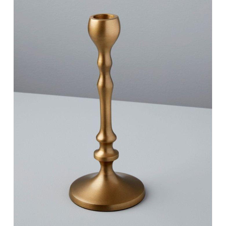 An aged bronze candlestick stands on a light gray surface against a pale gray background. This handcrafted piece features a smooth, curved design with a wide circular base and narrow top, perfect for holding one candle. Its metallic finish exudes the elegance of luxurious home essentials.