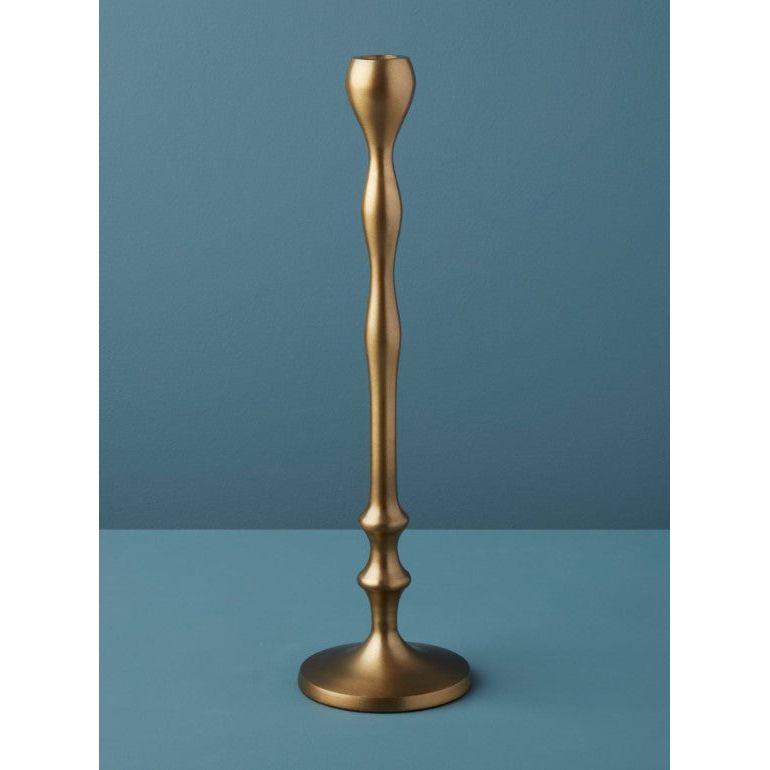 A sleek, modern candlestick holder, reminiscent of the Aged Bronze Candlestick, stands on a flat surface. This handcrafted piece boasts a gracefully sculpted, undulating column and a round base. Set against a solid teal backdrop, its elegant metallic sheen epitomizes luxurious home essentials.