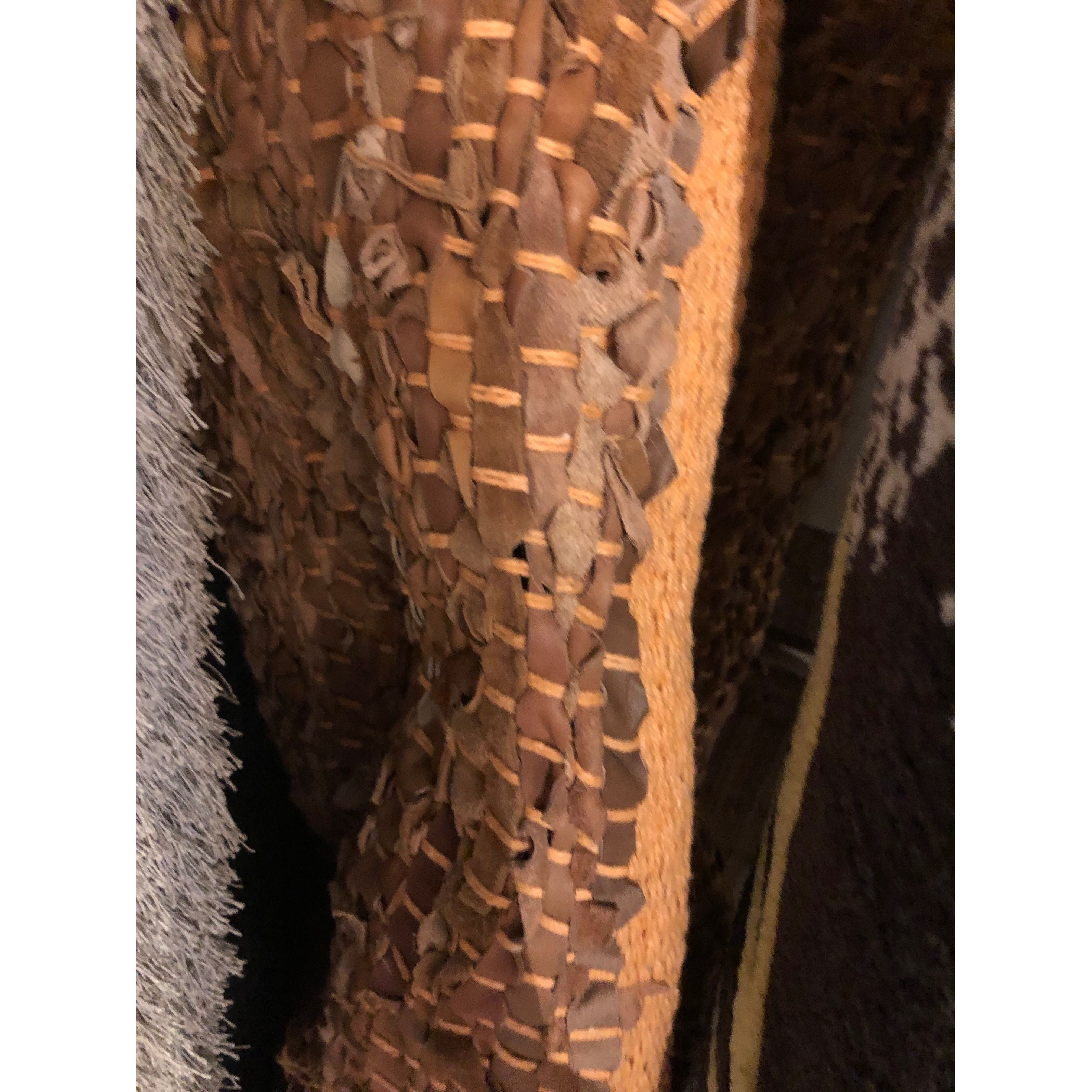 Close-up of a collection of fabrics featuring the Saket Rug, including a textured brown material with woven leather strips, a fluffy gray piece on the left, and a dark brown fabric on the right. The image showcases the contrasting textures and patterns of each fabric.