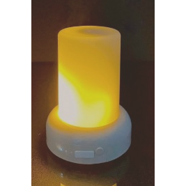 A Mini Rechargeable LED Candle glows warmly with a yellow hue, mimicking a realistic flame effect. The light sits on a white base featuring a power button and brightness control slider. In the dark background, the Mini Rechargeable LED Candle shines brighter, its glow reflecting off the surface beneath it.