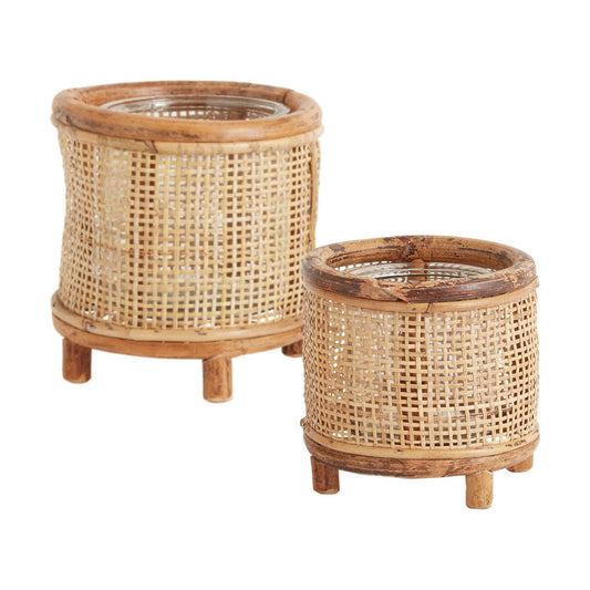 Two round, Wicker Candleholders in different sizes are displayed. Each holder boasts a cylindrical shape with woven wicker walls, wooden top and bottom edges, and three short wooden legs. The larger Wicker Candleholder is positioned slightly behind and to the left of the smaller one.