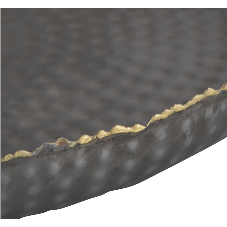 The Leonard Tray features a close-up of a textured metal surface, its grey finish showcasing a hammered pattern. The wavy gold rim elegantly enhances its sophisticated design against the gray metal background.