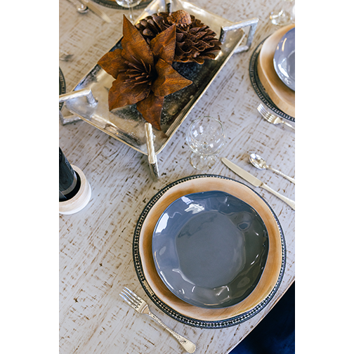 A rustic table setting with a gray plate on a tan charger, silverware, wine glass, and the Rust Aster Metal Flower centerpiece on a silver tray with pinecones atop a textured light wood table. Perfect for outdoor décor.