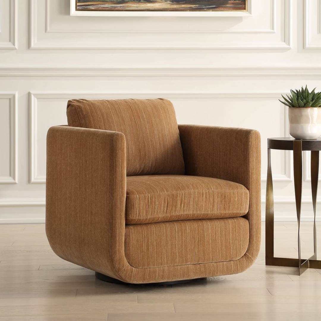 The Solana Swivel Accent Chair, Ginger in textured chenille features sculptural curves and sits on a light wood floor beside a round side table with a gold geometric base and potted plant. White paneled walls and framed art complete the space.