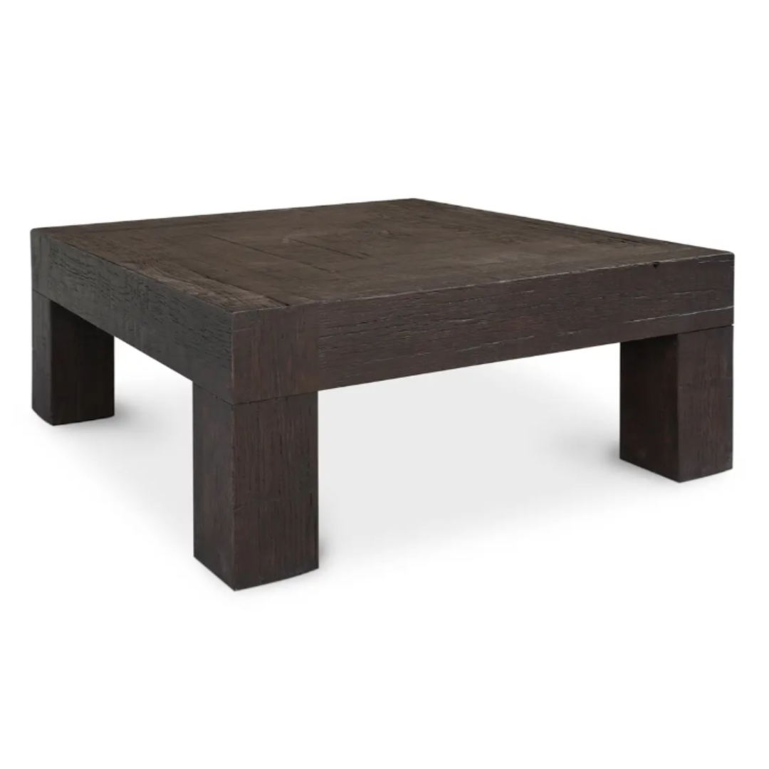 The Block Coffee Table in Rustic Brown is a square, dark brown piece crafted from reclaimed oak with thick legs and a smooth top. Its textured finish offers rustic charm, while the minimalist design enhances modern aesthetics against a plain white background.