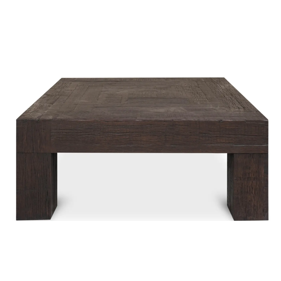 The Block Coffee Table in Rustic Brown is crafted from reclaimed oak and features a minimalist design with thick, sturdy legs. Its textured, rustic surface elegantly blends modern construction with timeless charm.