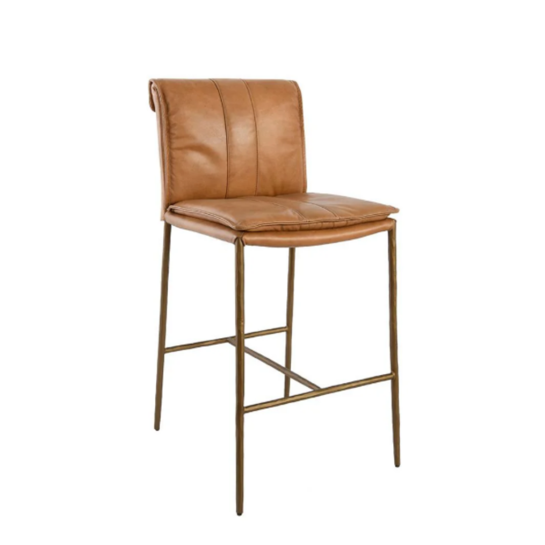 The Calder Leather Counter Stool is a tall barstool with a padded seat and backrest upholstered in tan leather. It features a sleek, sculptural metal frame with thin metallic legs in a bronze or brass finish, and the backrest's slight roll with vertical stitching enhances its subtle elegance.