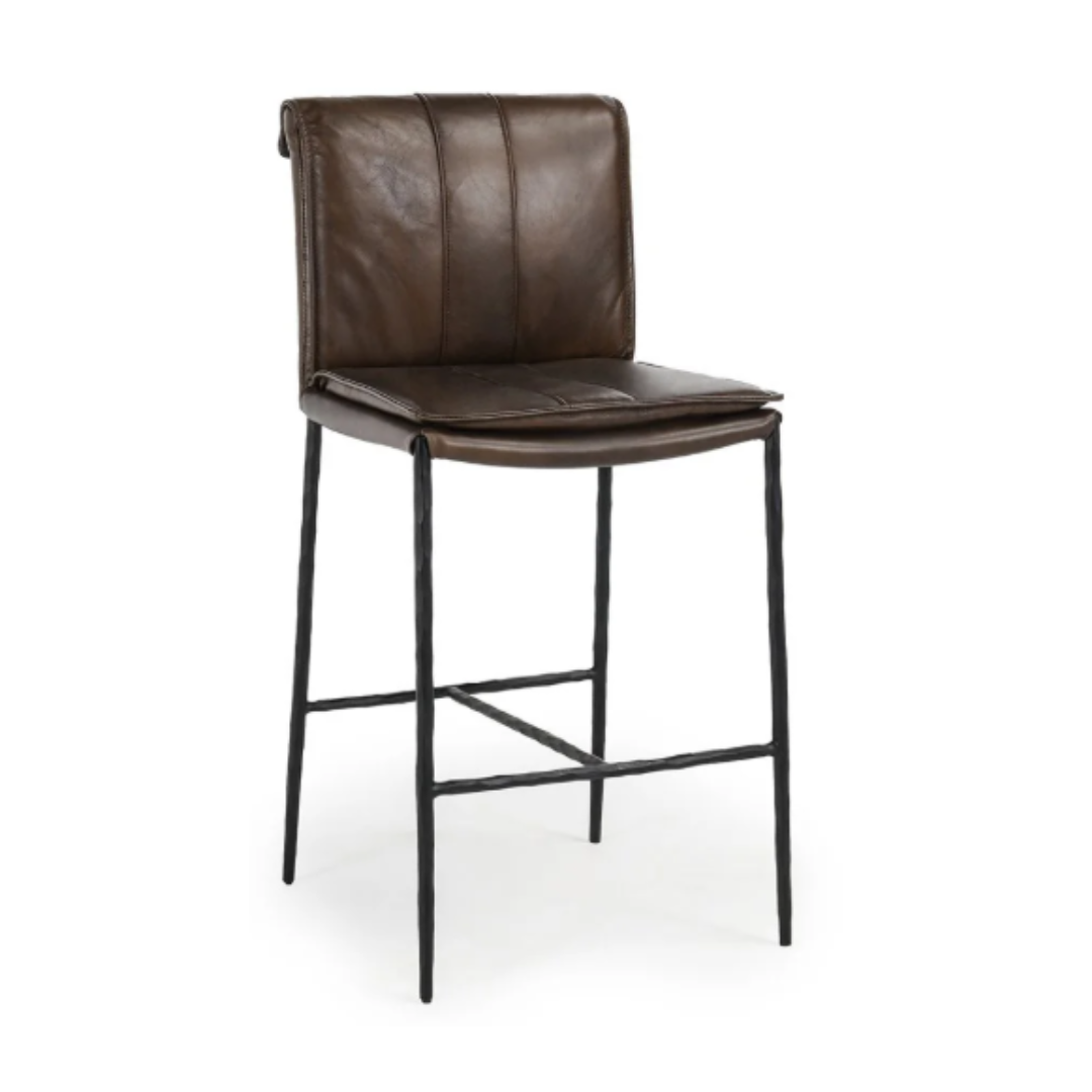 The Calder Leather Counter Stool features dark brown leather upholstery with a padded backrest and vertical stitching. Its sculptural metal frame showcases slender, textured black legs connected by a horizontal footrest, blending modern minimalism with industrial and classic styles.