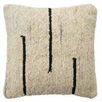 The Dillon Wool Pillow is a square, cream-colored cushion with a soft, textured weave and three uneven vertical black lines on the front, offering a modern, minimalist look. Plush and comfortable, it resembles a cream and black woven rug.