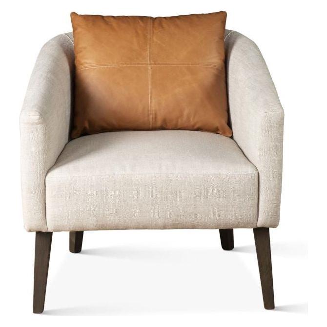 Introducing the Serenity Accent Chair, a chic addition to any space. This beige upholstered beauty, featuring wooden legs and a high backrest, embodies modern elegance. It comes with a square brown leather accent pillow placed on the seat, all set against a plain white backdrop that accentuates its minimalist charm.