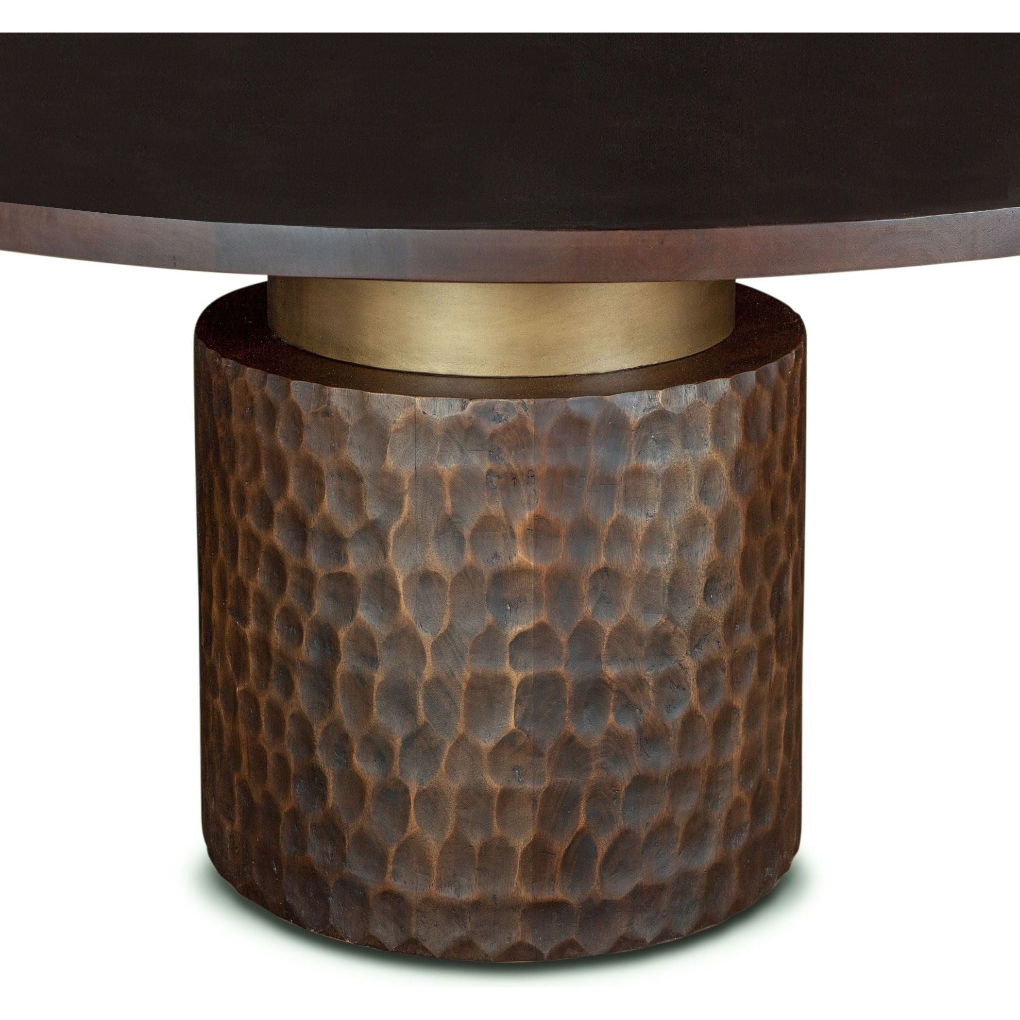 The Cruz 60" Round Dining Table features a two-toned design with a smooth, dark top and a cylindrical base made from hand-carved mango wood. The textured base has a hammered look and is adorned with a metallic band, offering a blend of contemporary and modern rustic styles.
