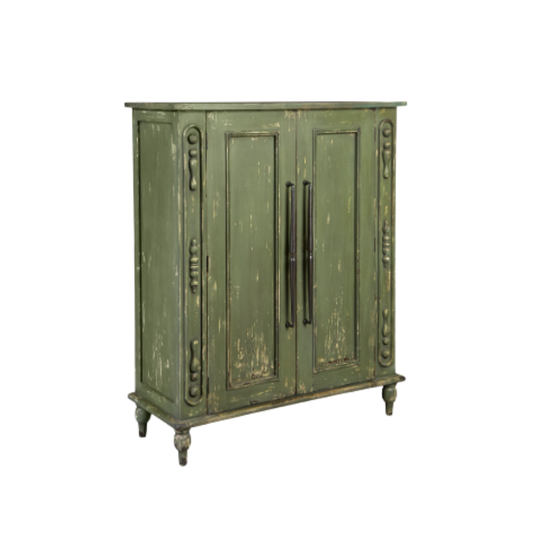 The Lorent Vintage Green Mahogany Cabinet exudes rustic charm with its distressed finish and intricate carvings. It features two paneled doors with dark metal handles and stands gracefully on four turned legs, combining functional elegance with antique allure.