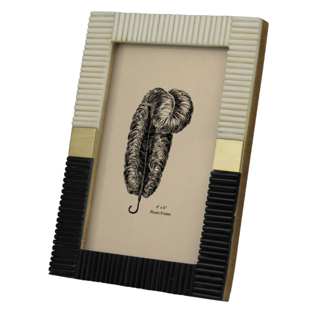 The Marcelle Two-Tone Photo Frame showcases a ribbed design with a white top, black bottom, and gold accents on the sides. This Art Deco-inspired frame, featuring a feather illustration, is perfect for displaying a 4x6 photo.