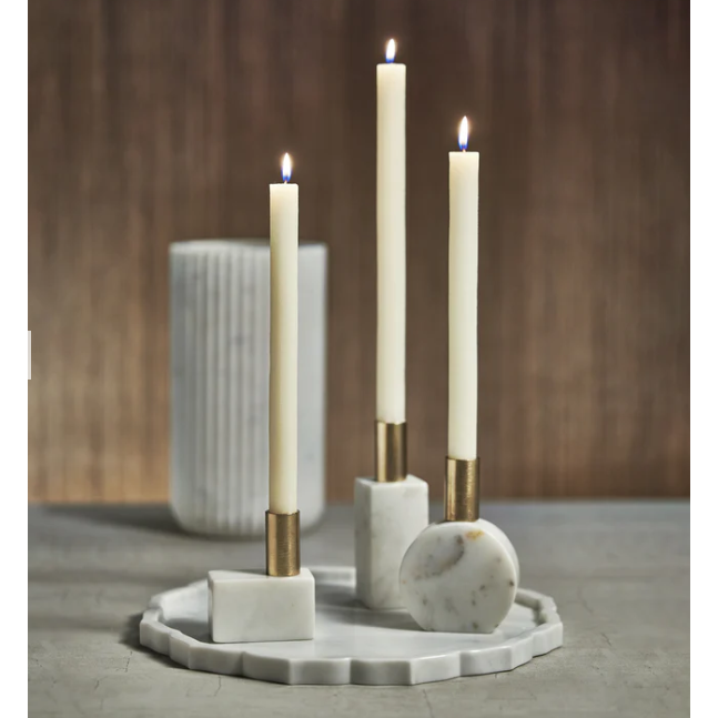 The Morphinan Marble Candle Holders (Set of 3) stylishly present three tall, lit white candles in marble holders with gold accents, elegantly positioned on a round, textured white tray. Behind them, a tall, ribbed cylindrical marble vase enhances the sophisticated arrangement, making it an ideal accent for luxurious home decor.