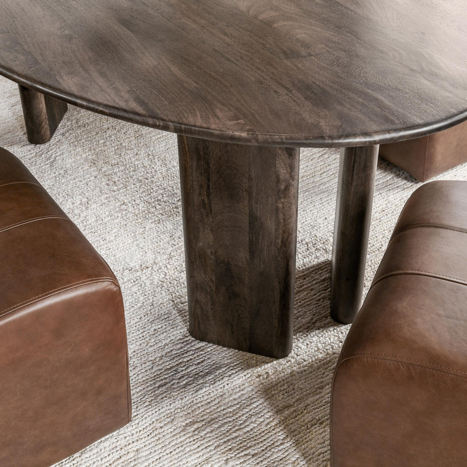 Wooden dining table with a textured surface and four legs, surrounded by brown leather chairs on a light gray carpet.