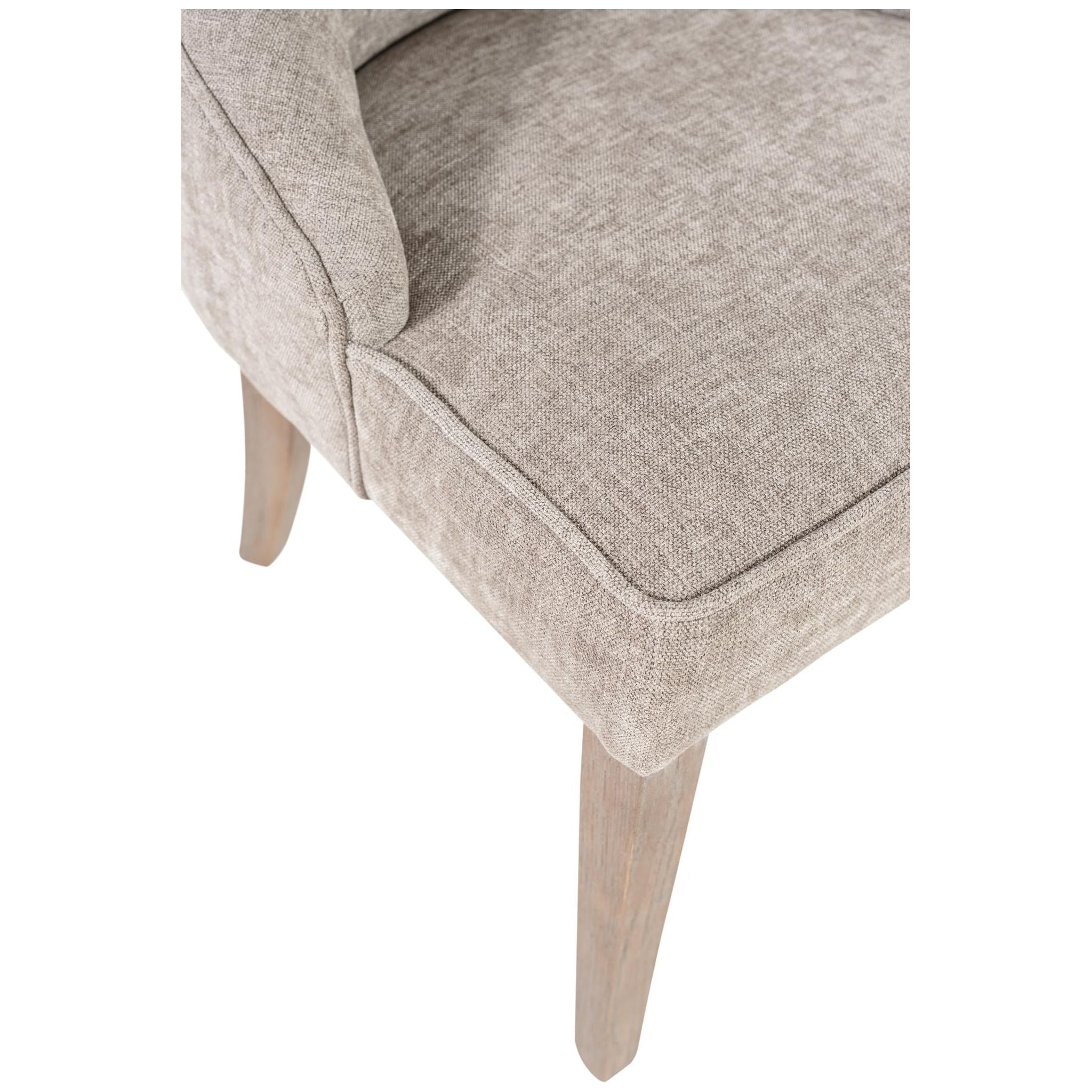 A close-up view of the Garet Dining Chair showcasing its beige upholstery with a subtle textured pattern and thick, comfortable seating cushion. The chair features reclaimed oak legs, and the top left corner reveals a glimpse of its armrest.