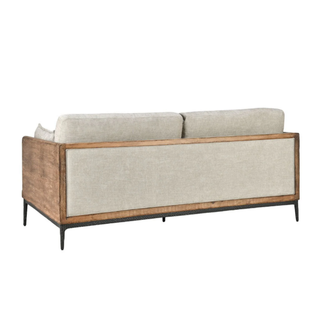 The Saville Upholstered Sofa features a beige couch with a reclaimed pine frame, showcasing light brown wood and visible grain. It includes two large backrest cushions, and its slim, dark tapered legs add to its modern look from the rear angled view.