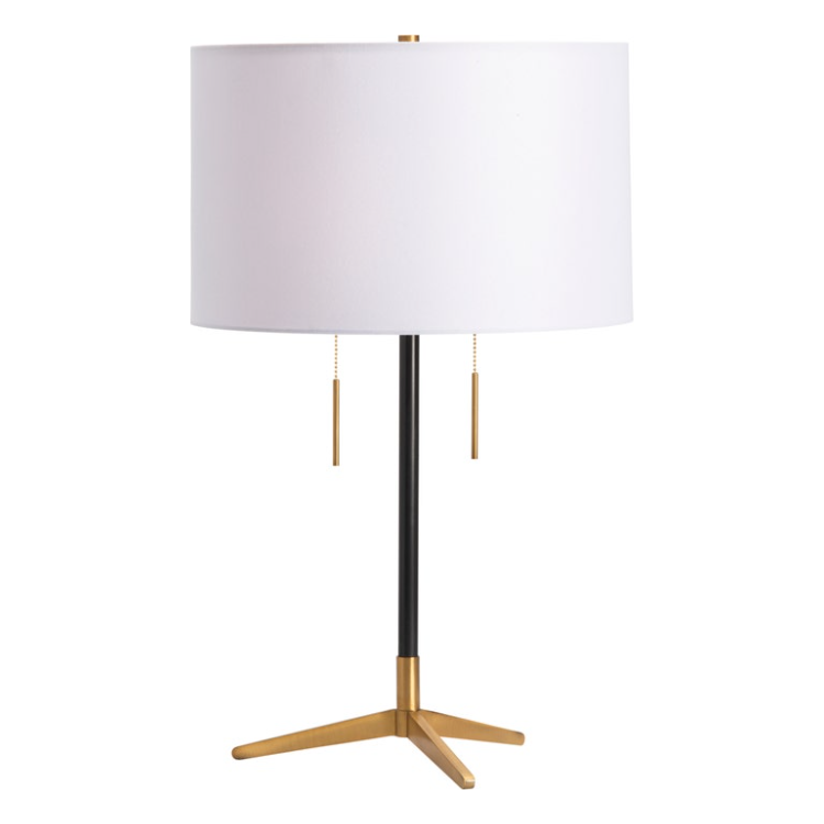 The Carson Table Lamp features a modern design with a large, white cylindrical shade and a sleek black stand. Its base is crafted from blackened bronze and boasts a tripod shape with three splayed legs. Two brass pull chains hang just below the shade for convenient operation, embodying a minimalist aesthetic with an elegant touch.