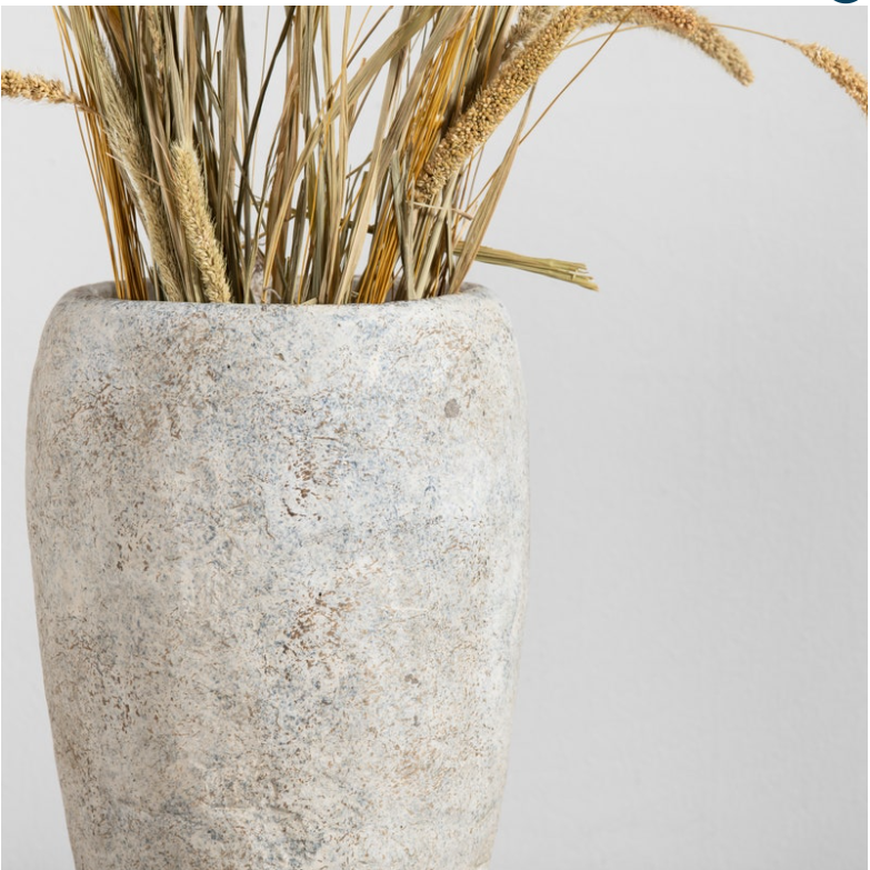 The La Palata Vase, made of textured cement, is filled with dried grasses and wheat stalks, set against a plain, light-colored background. This rustic home decor piece features a rough surface with botanicals in golden and beige hues, giving the arrangement a natural and minimalist aesthetic.