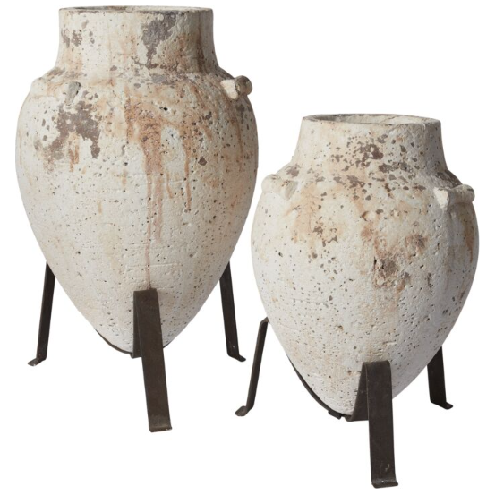 Perched on Tuscan Plant Stands, the large weathered white clay urns radiate artisanal charm, showcasing a rough textured surface. These vintage-inspired urns, featuring handles on each side and notable patches of brown discoloration, embody an aged, rustic aesthetic.