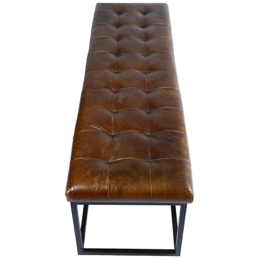 The Northwood Bench showcases a brown, button-tufted leather seat with a gently distressed look that enhances its rustic appeal. Its minimalist black metal base merges modern and vintage elements, ensuring it complements a wide range of interior styles.