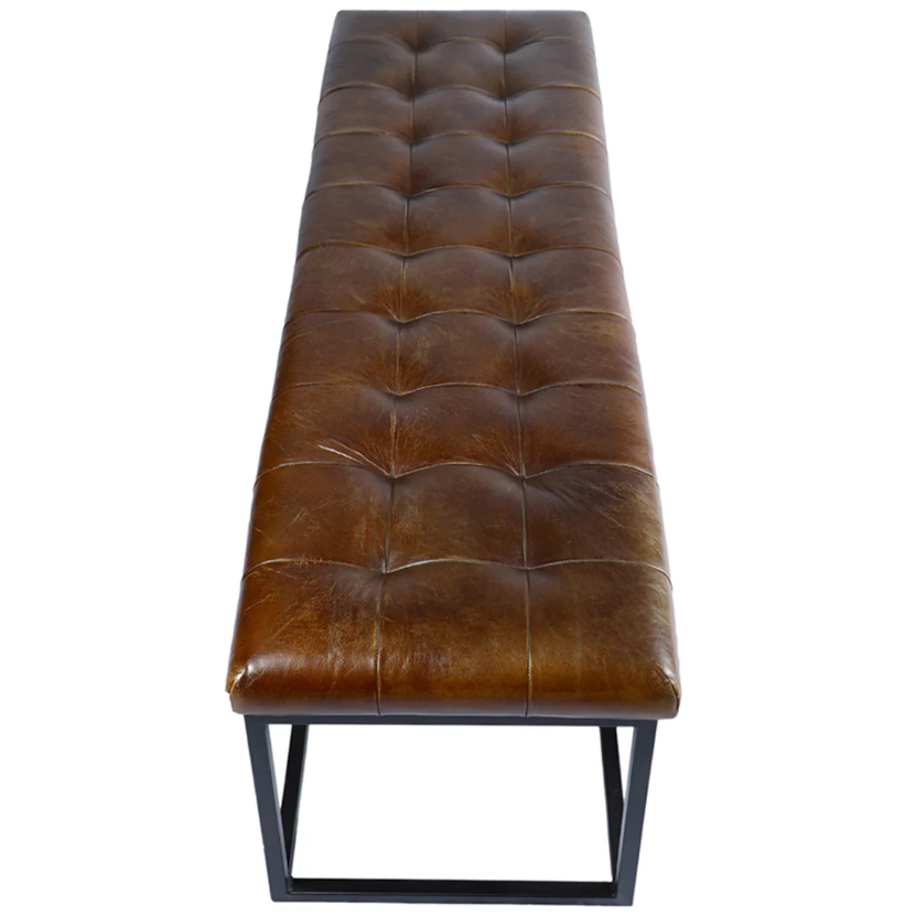 The Northwood Bench showcases a brown, button-tufted leather seat with a gently distressed look that enhances its rustic appeal. Its minimalist black metal base merges modern and vintage elements, ensuring it complements a wide range of interior styles.