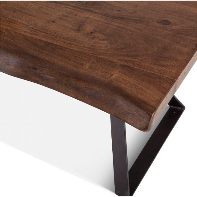 A close-up of the Loft Natural Live Edge Coffee Table corner highlights its Acacia wood tabletop, showcasing visible grain patterns and knots. The edge maintains the natural shape of the wood with an uneven finish. It is supported by a sturdy, black, rectangular metal leg that adds an industrial touch.