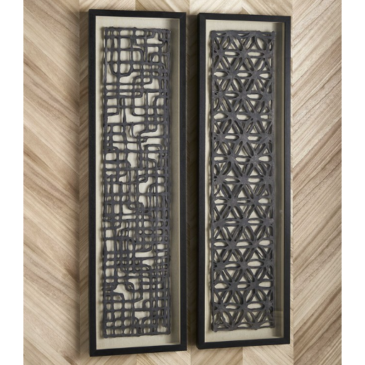 Two pieces of framed wall art from the Evander Wall Art collection feature intricate black patterns on beige backgrounds. The left frame displays an abstract grid-like design, while the right illustrates a geometric pattern with interlocking hexagons. Both shadow box frames are showcased against a wooden, herringbone-patterned wall.