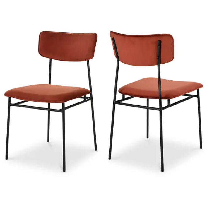 Two Elara Amber Dining Chairs, showcasing a minimalist design. Each chair features an armless structure with a sleek black metal frame and rust-red, foam-padded seat cushions. One chair is presented from the front, while the other is shown from the back, accentuating its clean and simple lines.