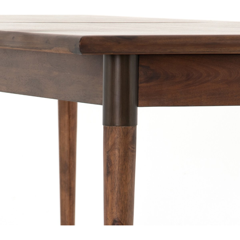 Close-up of the Teresa Extension Dining Table corner showcasing its rich toasted walnut finish. The table features cylindrical, tapered legs with a darker-colored joint connecting them to the tabletop. The detailed wood grain and smooth finish are prominently visible, giving the piece a rustic yet refined appearance inspired by Scandinavian modernism.