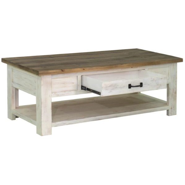 The Provence Coffee Table is a rustic, rectangular piece crafted from reclaimed FSC pine. It boasts a spacious tabletop with a natural wood finish, complemented by a whitewashed base. The table features a visible drawer with a black handle, partially pulled out on one side, and includes a lower shelf for extra storage or decor, enhancing its rustic charm.