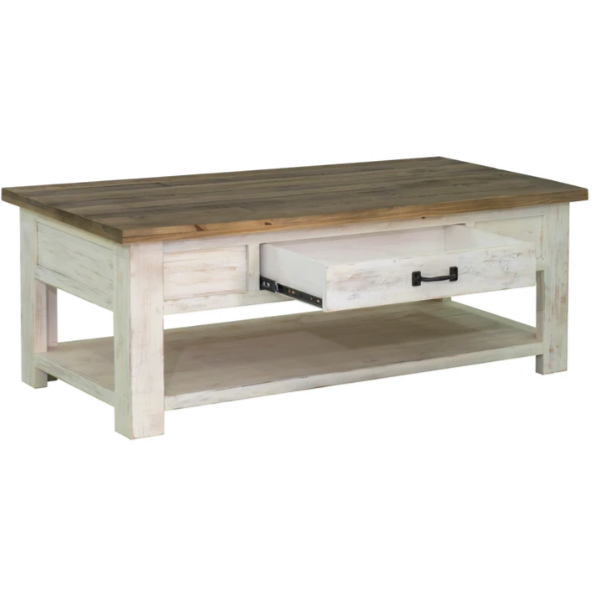 The Provence Coffee Table is a rustic, rectangular piece crafted from reclaimed FSC pine. It boasts a spacious tabletop with a natural wood finish, complemented by a whitewashed base. The table features a visible drawer with a black handle, partially pulled out on one side, and includes a lower shelf for extra storage or decor, enhancing its rustic charm.